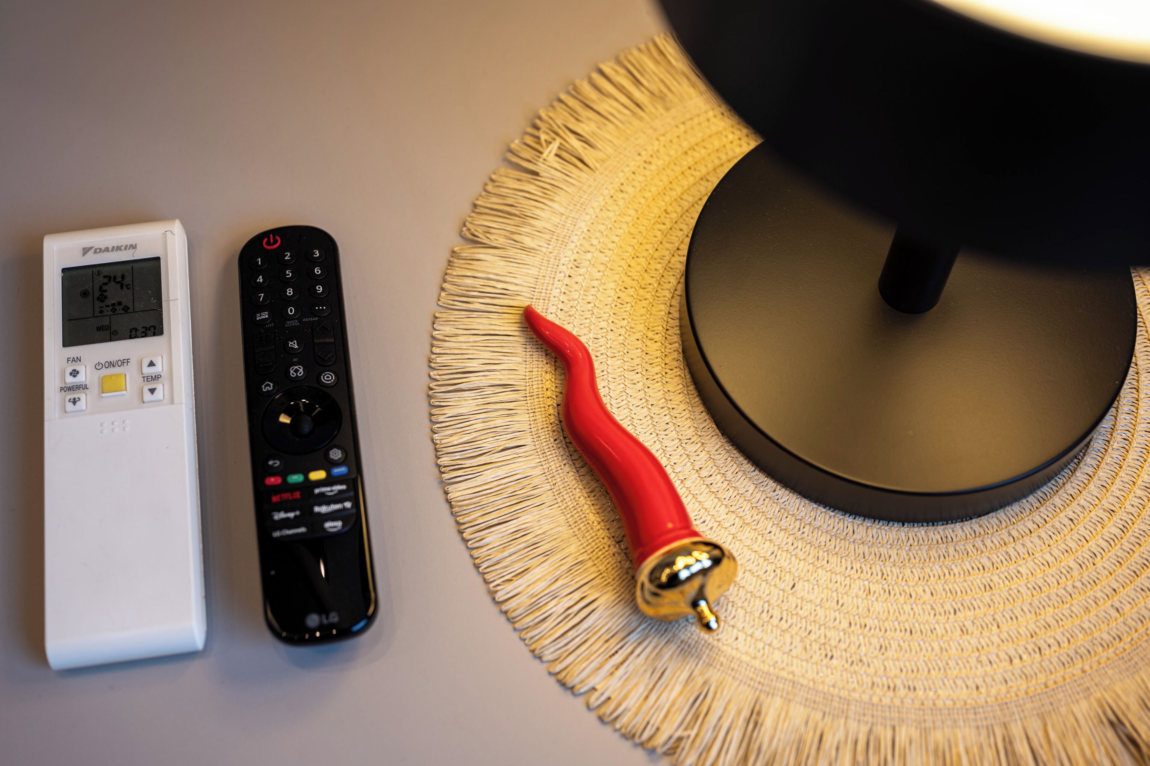A white thermostat, a black remote control, and a red decorative item on a textured surface.