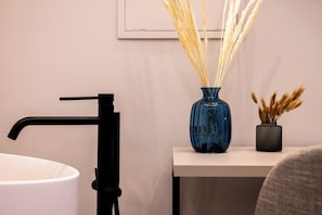 A bathroom with a white sink, a black faucet, and a blue vase with dried plants on a white countertop. - Plebiscito Luxury Guest House (Naples)