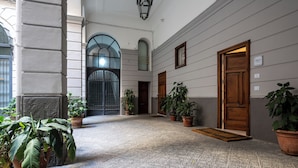Um corredor com chão de azulejos, plantas em vasos e uma porta de madeira.