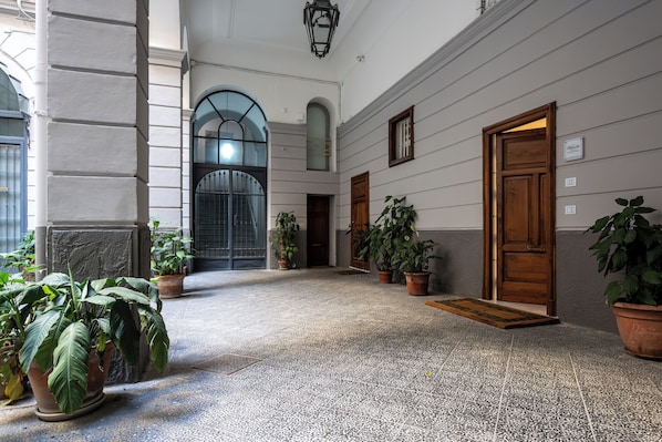A hallway with a tiled floor, potted plants, and a wooden door. - Plebiscito Luxury Guest House (Naples)