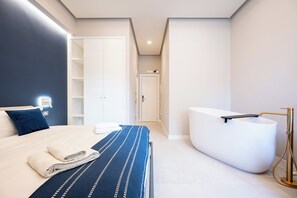 Une chambre à coucher moderne avec un grand lit, une baignoire intégrée et un dressing.