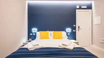 Una cama bien hecha con una colcha a rayas azules y blancas, dos almohadas amarillas brillantes y toallas dobladas a cada lado.