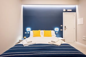 A neatly made bed with a blue and white striped bedspread, two bright yellow pillows, and folded towels on either side. - Plebiscito Luxury Guest House (Naples)