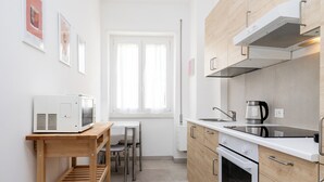 A modern kitchen with a microwave, stove, and sink. There is a window with curtains, a wooden table, and a shelf. - Dimora Aniene (Rome)