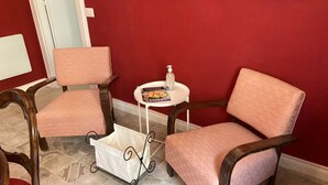 Een kamer met twee roze fauteuils, een klein wit tafeltje met een tijdschrift en een fles, en een witte kinderwagen.