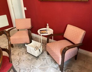 Een kamer met twee roze fauteuils, een klein wit tafeltje met een tijdschrift en een fles, en een witte kinderwagen.