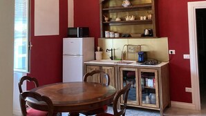 Een eetruimte met een houten tafel en stoelen, een witte koelkast, een magnetron, een kast met keukengerei en een kroonluchter.