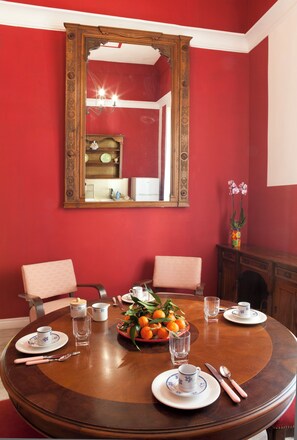 Ein Esszimmer mit einem runden Tisch, gedeckt für vier Personen, einem großen, verzierten Spiegel darüber und einer Vase mit Blumen auf einem Beistelltisch.