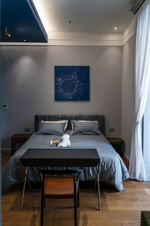 Un dormitorio moderno con cama, mesitas de noche, un escritorio y un amplio ventanal con cortinas.