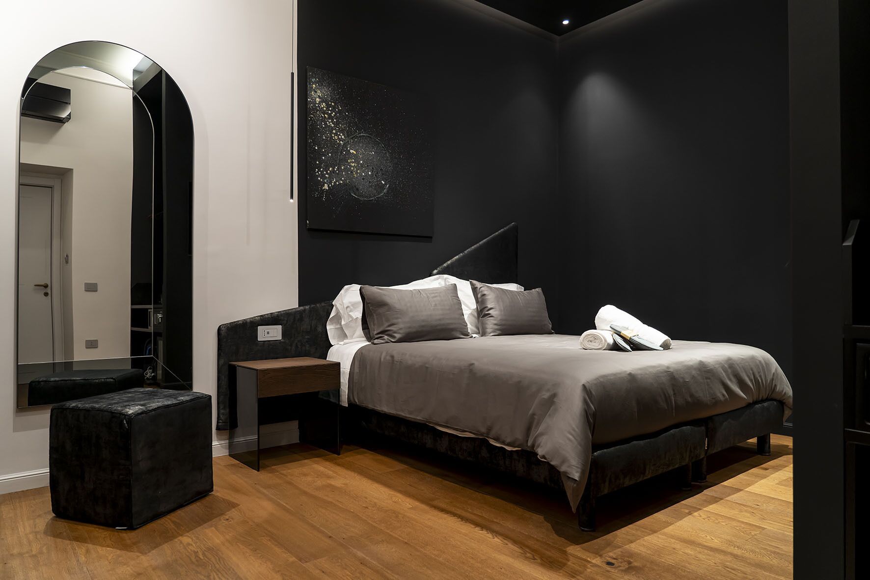 Ein modernes Schlafzimmer mit Bett, Nachttischen, einem großen Spiegel und einer dunklen Wand mit strukturierter Kunst.
