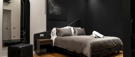 A modern bedroom with a bed, bedside tables, a large mirror, and a dark wall with a textured artwork.