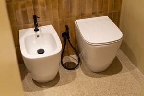 A bathroom with a bidet, a toilet, and a floor with speckled tiles. - Via Chiaia 123 - Camera Oltremare (Naples)