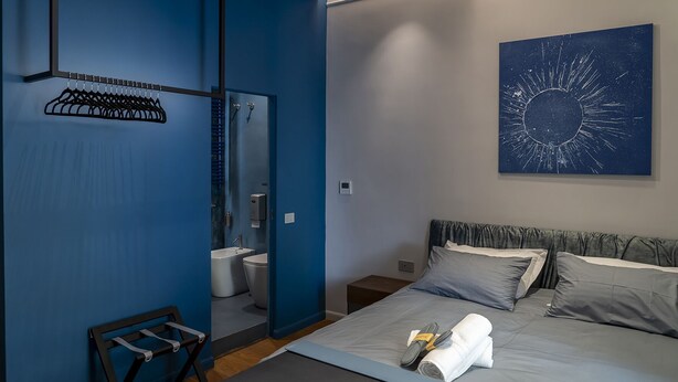 A modern hotel room with a bed, a bathroom, a mirror, and a wall art piece. - Via Chiaia 123 - Camera Oltremare (Naples)