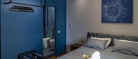 A modern hotel room with a bed, a bathroom, a mirror, and a wall art piece.