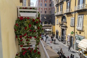 A balcony with red flowers, a street with pedestrians, and buildings with balconies. - Via Chiaia 123 - Camera Oltremare (Naples)