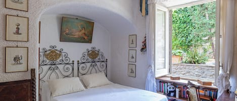 A bedroom with a bed, a window with curtains, a bookshelf, and a wall with framed pictures.