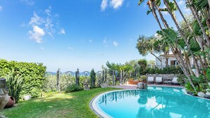 Piscina privativa com borda curva, rodeada por vegetação exuberante e céu azul.