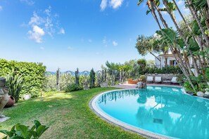 A private pool with a curved edge, surrounded by lush greenery and a clear sky. - Complesso Villa Le Palme (Forio)