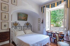 Un dormitorio con una cama, una ventana con cortinas, una estantería y un cuadro en la pared.