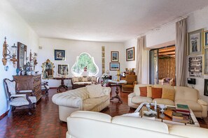 A spacious living room with a large window, a sofa, a chair, a coffee table, and a bookshelf. - Complesso Villa Le Palme (Forio)