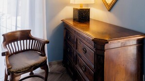 Ein Eckzimmer mit Holzstuhl, Schreibtisch mit Schubladen, Lampe und gerahmten Bildern an der Wand.