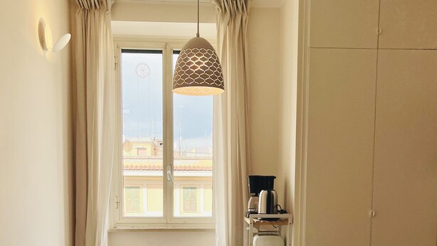 Comedor con una mesa preparada para cuatro, sillas verdes, lámpara colgante y vista a edificios a través de una ventana.