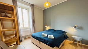 Un dormitorio moderno con una cama, lámparas de noche, un armario de madera, una silla y un radiador.