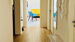 Un pasillo con piso de madera, un banco blanco y un sofá amarillo al fondo.