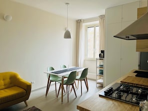 A modern kitchen with a gas stove, a dining table with chairs, a yellow sofa, and a window with curtains. - Casa Duci (Rome)