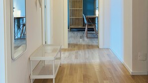 Un pasillo con un banco blanco, piso de madera, pared azul y un armario con perchero.