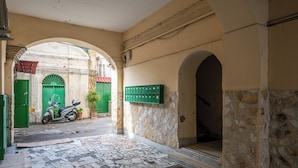 A narrow alleyway with a scooter parked at the entrance, a green mailbox, and a stone wall. - Casaré (Naples)