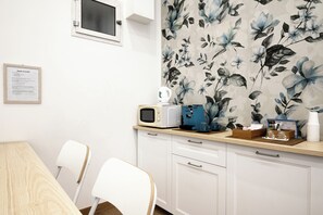 Una cocina con microondas, cafetera y un papel tapiz floral. Hay armarios blancos y una encimera de madera.