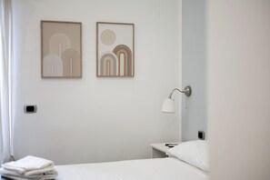 Habitación de hotel minimalista con cama, mesita de noche, lámpara y dos obras de arte abstracto en la pared.