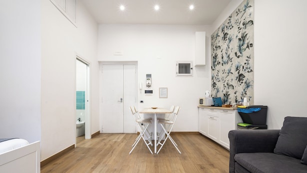A modern living room with a sofa, a dining table with chairs, a kitchen area, and a bathroom visible through an open door. - Casaré (Naples)