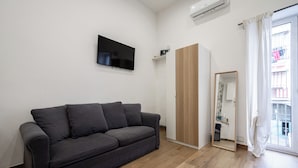A modern living room with a grey sofa, a mounted TV, a wooden wardrobe, and a large window with curtains. - Casaré (Naples)