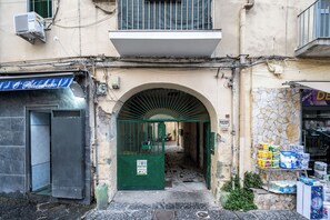 A narrow alleyway with a green gate, a stone wall, and a shop selling toilet paper. - Casaré (Naples)