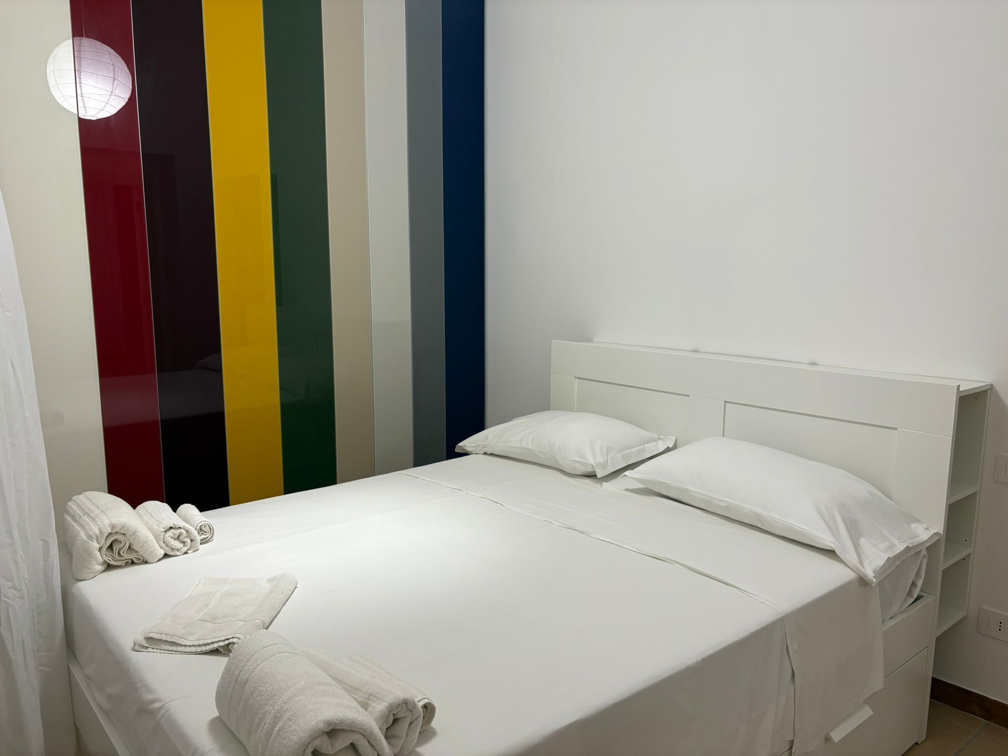 Ein Bett mit weißen Laken, einem Kopfteil und zwei Kissen. Handtücher liegen auf dem Bett.