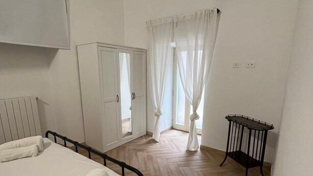 A hotel room with a bed, a wardrobe, a bedside table, and a window with curtains. - Casa Delle Camelie (Naples)