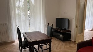 A living room with a wooden dining table, chairs, a television, and a red sofa. - Casa Delle Camelie (Naples)