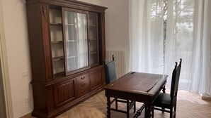 A dining area with a wooden table and chairs, a large wooden cabinet, and a hanging light fixture. - Casa Delle Camelie (Naples)