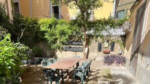 A courtyard with a table and chairs, surrounded by buildings and greenery. - Casa Delle Camelie (Naples)