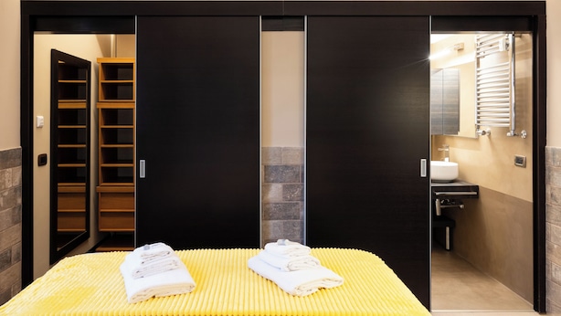 Ein Hotelzimmer mit Bett, Kleiderschrank und einem durchgegangenen Tür sichtbaren Badezimmer.