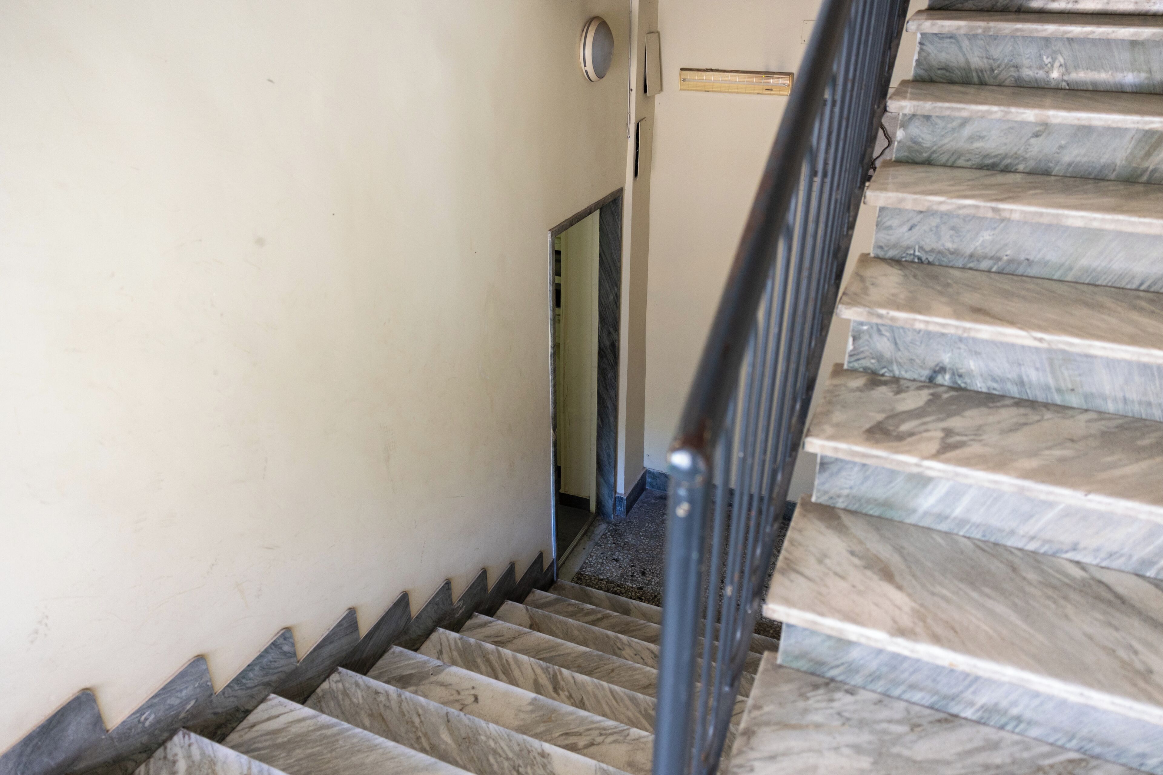 Un escalier avec des marches en marbre et une rampe métallique, menant à une porte.