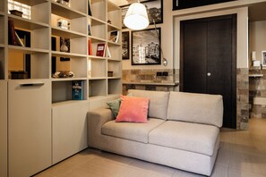Una sala de estar con un sofá, estanterías llenas de libros y objetos decorativos, una chimenea y una puerta oscura.