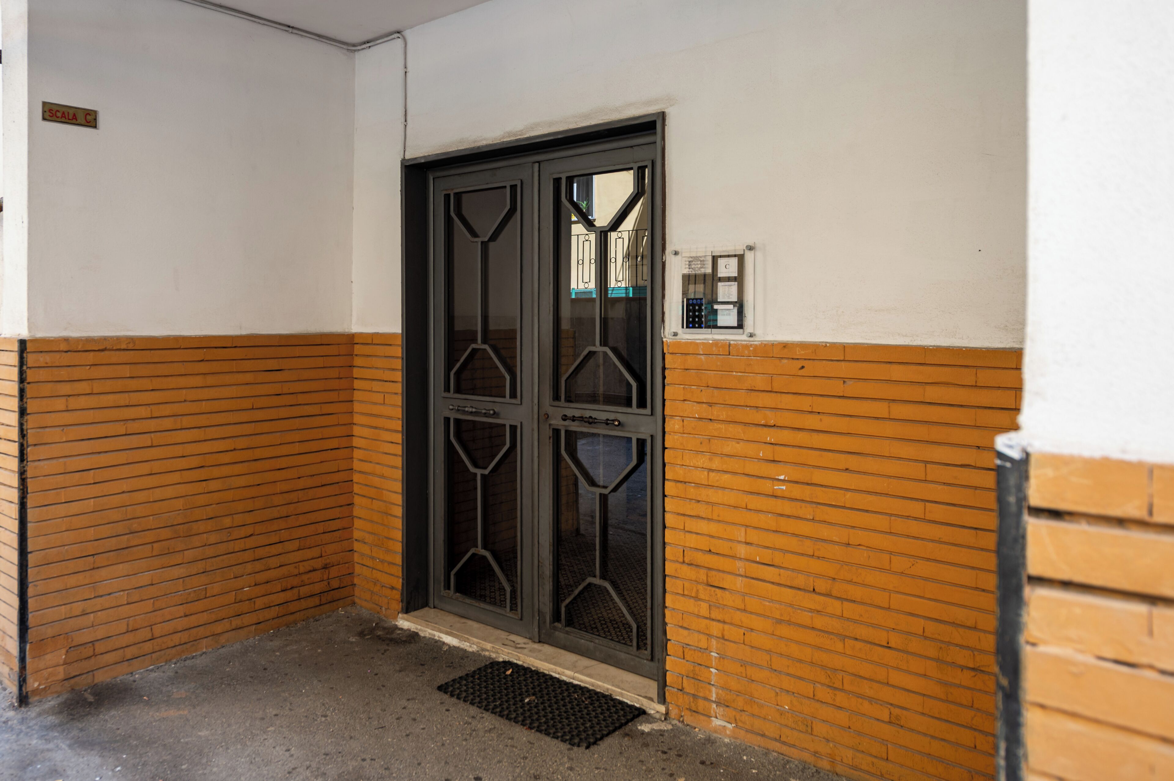 A door with a metal handle and glass panels, a small window with a security device, and a metal mat at the door's base.
