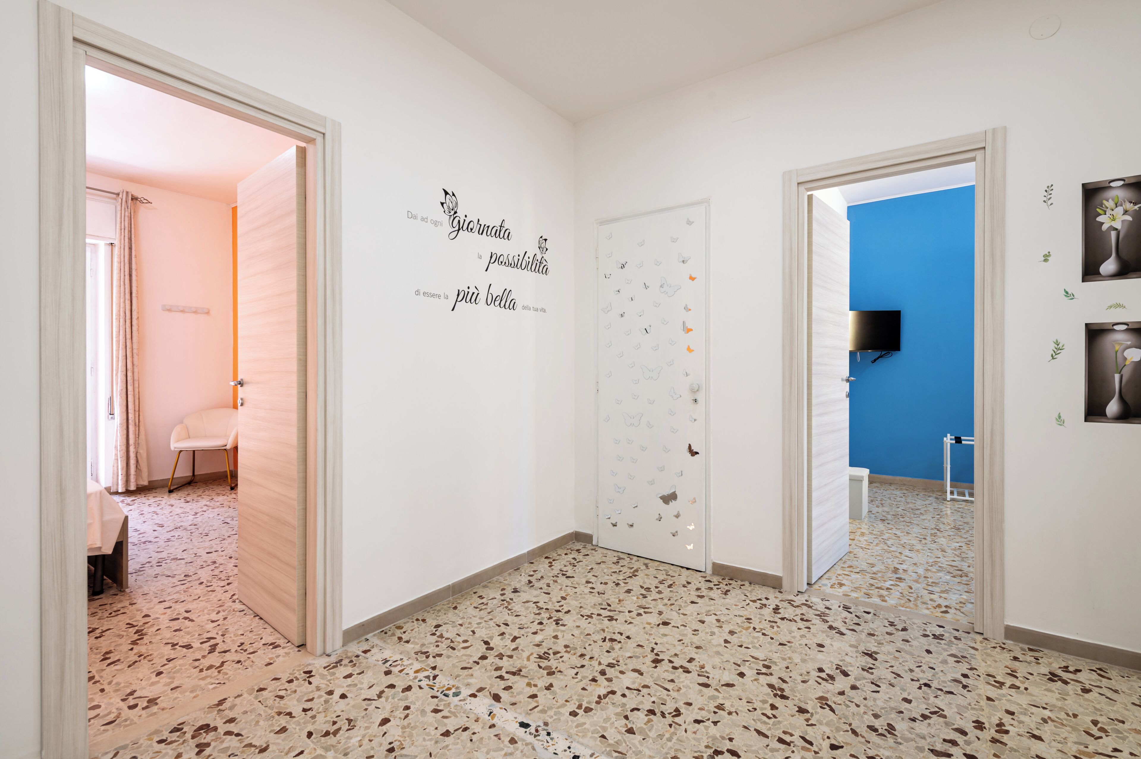 Un couloir doté d’un sol en terrazzo, de murs blancs et d’un mur d’accent bleu. On y trouve des autocollants décoratifs et un téléviseur à écran plat fixé au mur bleu.