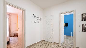 Un couloir doté d’un sol en terrazzo, de murs blancs et d’un mur d’accent bleu. On y trouve des autocollants décoratifs et un téléviseur à écran plat fixé au mur bleu.