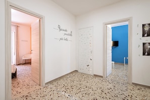 Um corredor com piso de terrazzo, paredes brancas e uma parede azul decorativa. Há adesivos decorativos na parede e uma televisão de tela plana presa à parede azul.
