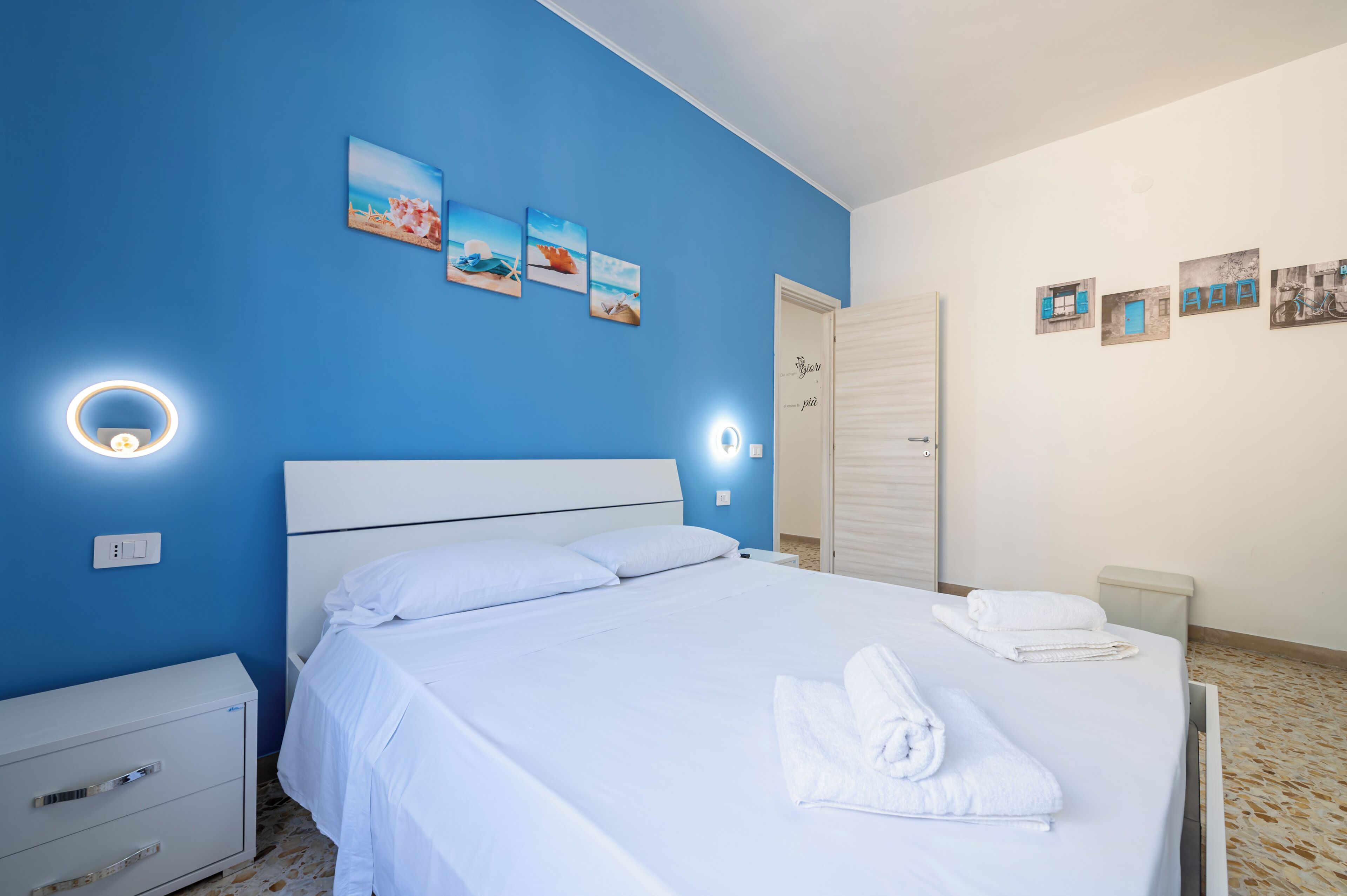 A hotel room with a large bed, a nightstand, a wardrobe, and wall art.
