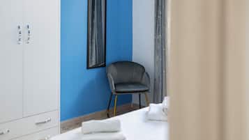 Habitación de hotel con una pared azul de acento, un sillón tapizado en gris, una mesa blanca con toallas dobladas y un espejo grande.